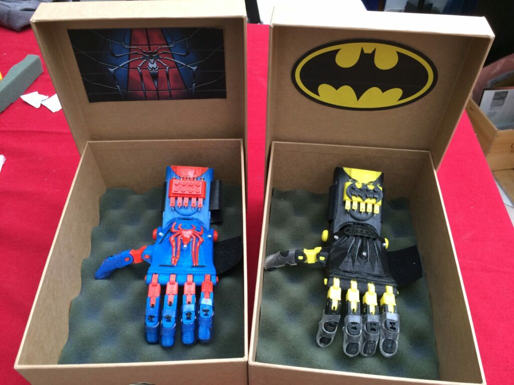 Deux prothèses de main : une bleue et rouge avec le logo de Spiderman, l'autre noire et jaune avec le logo de Batman.